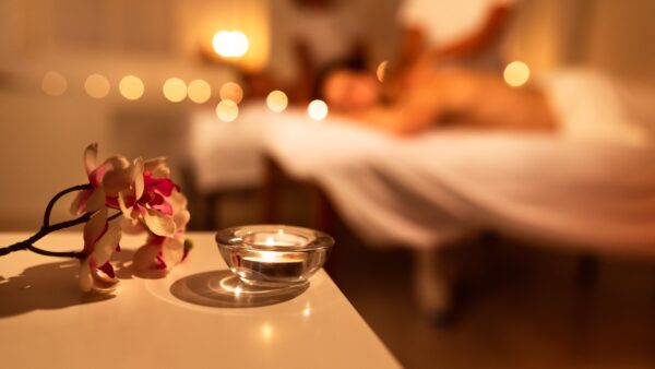 Creme per massaggi Lovibes – atmosfera sensuale con coppia distesa su lettino, luce soffusa, candela accesa e fiore profumato in primo piano