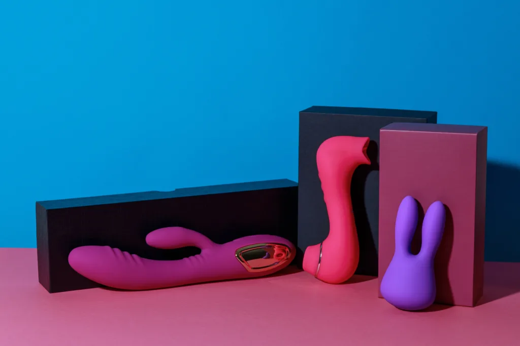 Sex toys colorati su sfondo rosa e blu: vibratori rabbit, stimolatori clitoridei e packaging elegante, simbolo di design moderno e piacere consapevole.