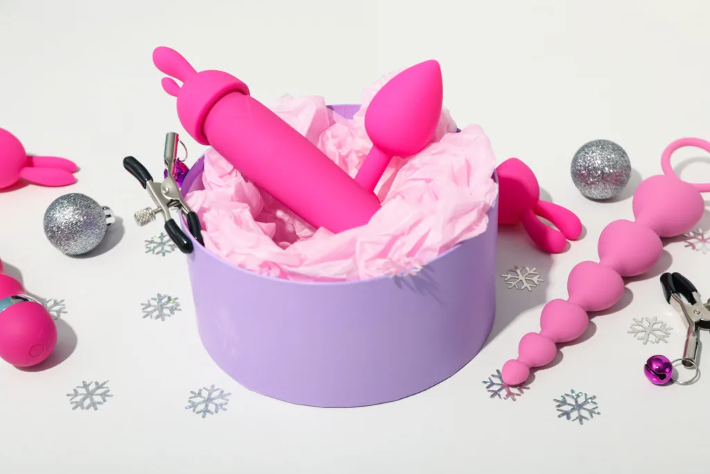 Sex toys rosa in confezione regalo lilla con carta velina, circondati da decorazioni brillanti e natalizie