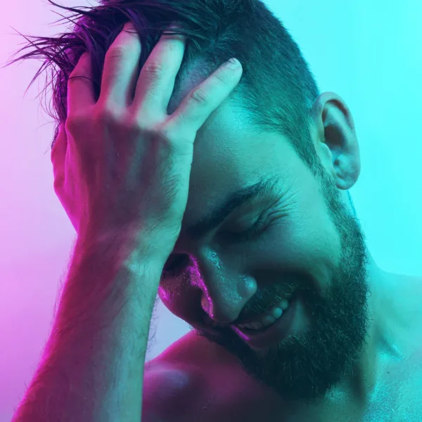Uomo giovane e sensuale con pelle bagnata illuminato da luce al neon, simbolo di piacere maschile e stimolazione della prostata in chiave erotica ed elegante